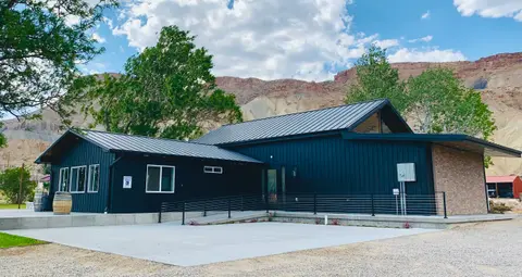 A modern black building stands against a backdrop of rocky hills and a blue sky with clouds.