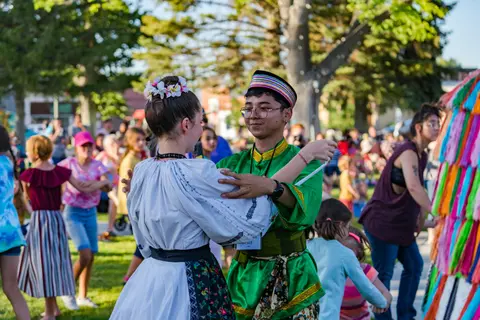 Two people in traditional folk costumes dance outdoors.