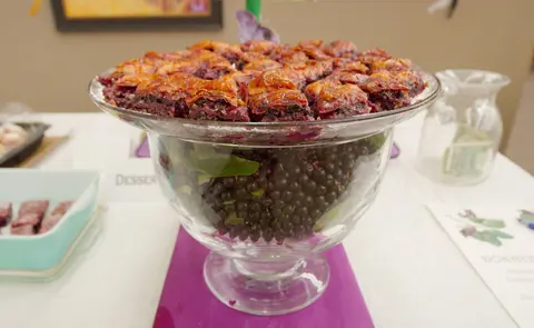 A large glass bowl filled with dark berries and topped with pastries on a table.