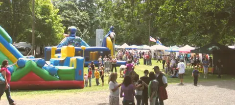 A crowd of people enjoying an outdoor fair with bounce houses and tents.