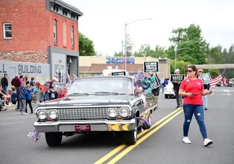 A vintage convertible car drives down a street in a parade.