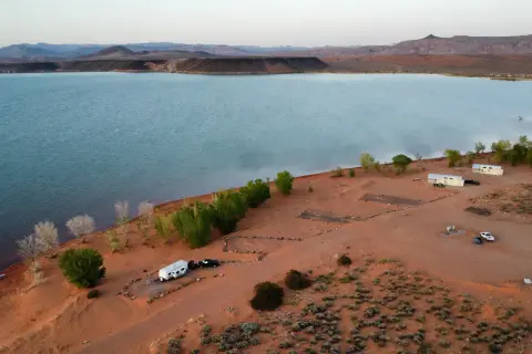 An aerial view of a lake and shoreline with a campground, trees, and RVs.