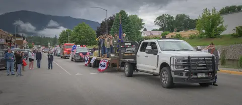 A parade float with veterans stands on a street with mountains in the background.