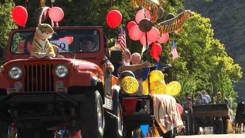 A red Jeep in a parade decorated with balloons, tiger figures, and flags.