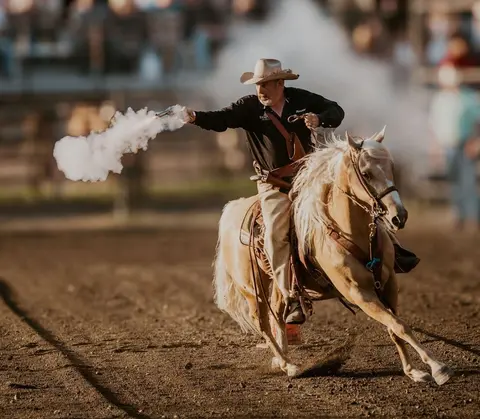A man rides a horse and shoots a gun, creating a cloud of smoke.