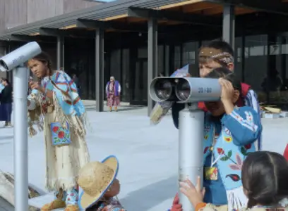 People looking through public viewing binoculars outside a building.