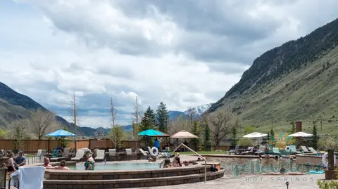People enjoy outdoor hot spring pools surrounded by mountains under a cloudy sky.