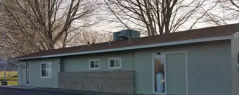 An exterior view of a single-story light green building with bare trees behind it.