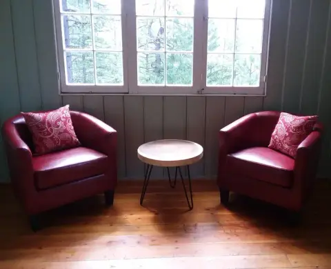 Two red armchairs and a small table sit in front of a window indoors.
