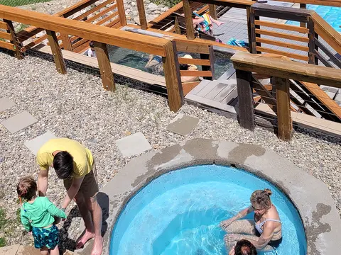An overhead view shows people enjoying a pool and hot tub with wooden decks.