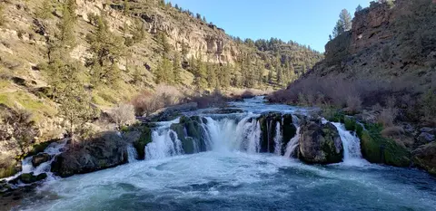 A scenic waterfall flows between rocky, tree-covered canyon walls.