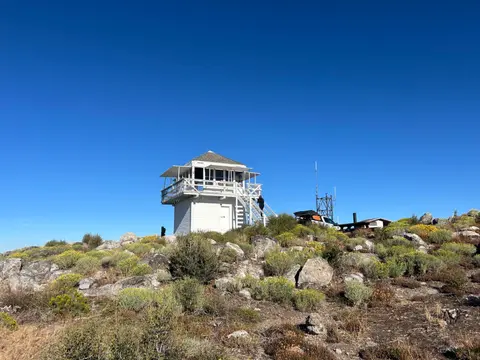 A white lookout tower stands on a rocky hillside under a clear blue sky.