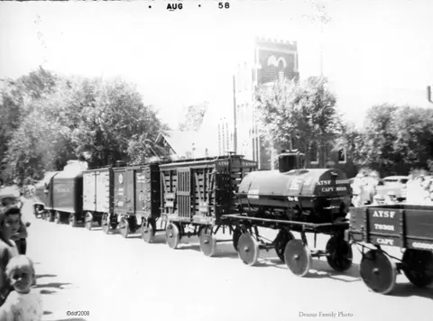 A black and white historic photograph showing a miniature train float on a street.