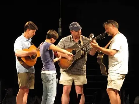 Four musicians play acoustic guitars on stage.