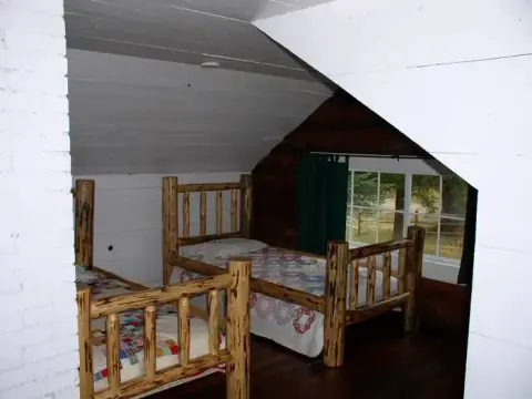 A rustic bedroom with two wooden log beds under a slanted white ceiling.