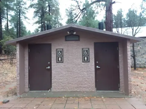 A public restroom building stands outdoors among trees.