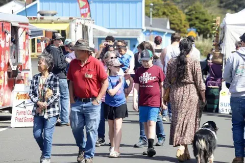 A crowd of people walks along a street past food trucks and tents.