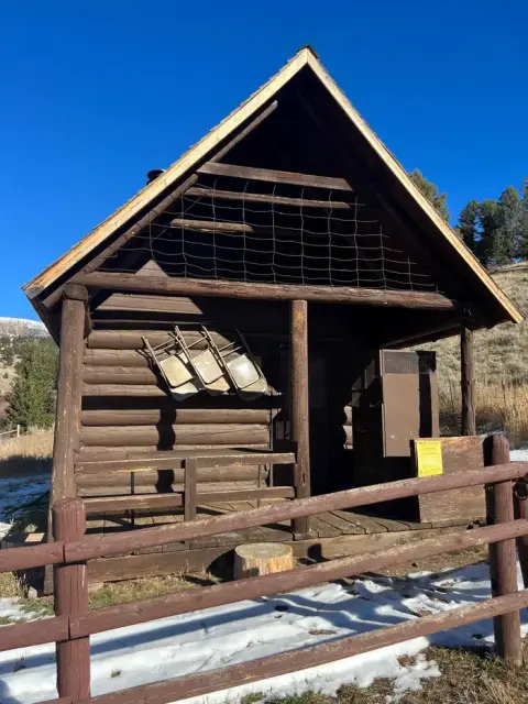 A small log cabin with a wooden porch sits outside against a clear blue sky.