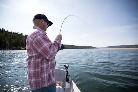 A man fishes from a boat on a lake.