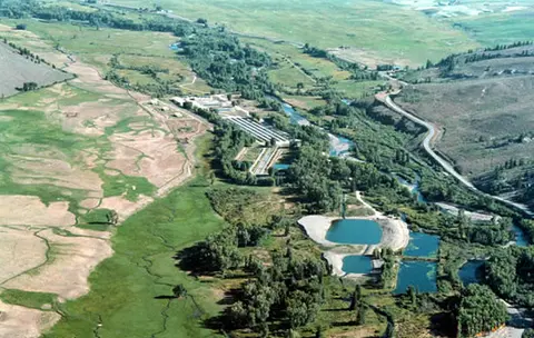 An aerial view shows a river valley with ponds and green fields.