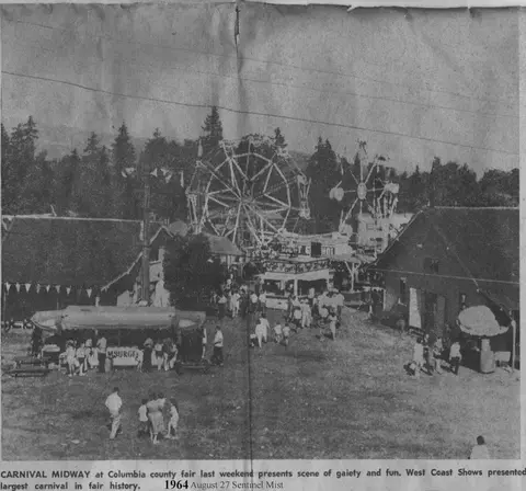 A black and white newspaper photograph showing a carnival midway with rides and people.