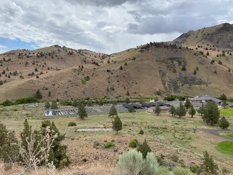 An elevated view of a facility in a valley surrounded by dry hills under a cloudy sky.