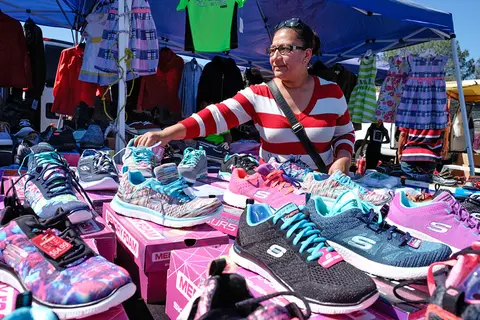 A woman browses shoes at an outdoor market stall.