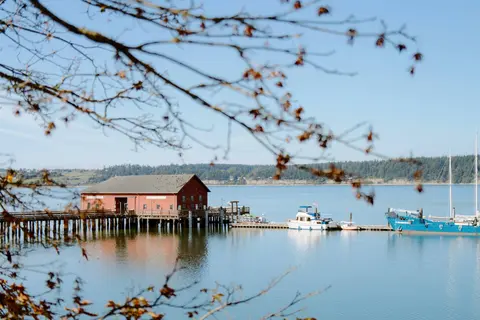 A red building on a wooden pier by the water with boats docked alongside.