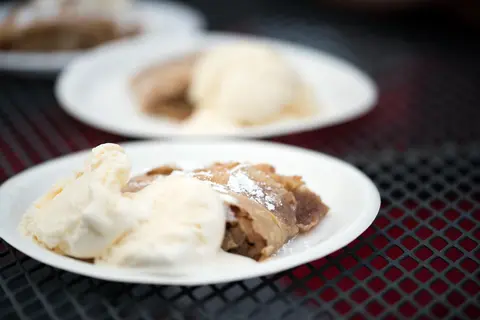 Plates of strudel with ice cream served on a mesh table.