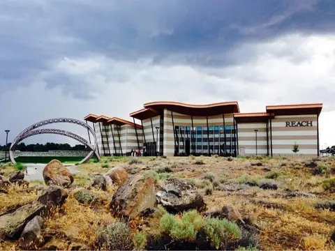 Exterior view of a modern building with a curved roof and an outdoor sculpture under a cloudy sky.