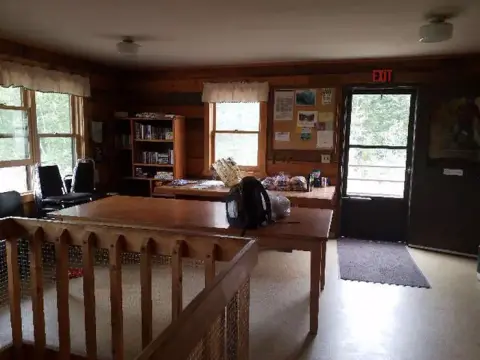 An interior view of a rustic log building with wooden tables, a bookshelf, and an exit door.