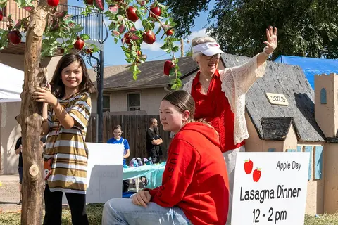 People gather outdoors near a decorated display with an event sign.