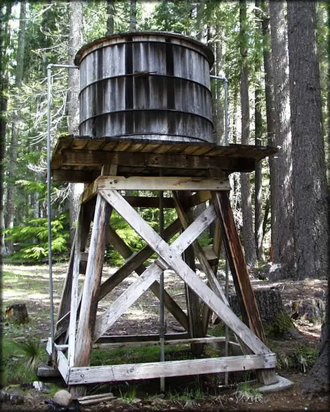 A wooden water tower stands among trees in a forest.