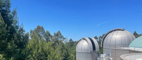 A view of observatory domes among trees under a clear blue sky.