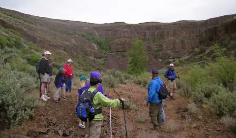 A group of hikers stands on a trail in a rugged, rocky canyon.