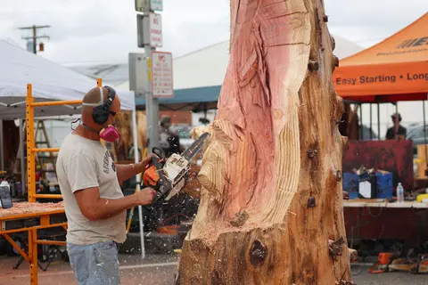 A man uses a chainsaw to carve a large wooden log outdoors.