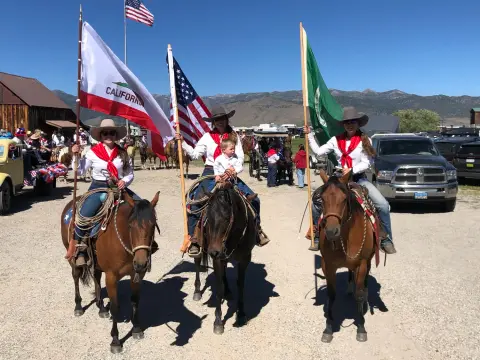 Three people on horseback holding flags pose outdoors.