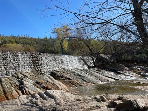 A stone dam spilling water over rocky terrain under a clear blue sky.