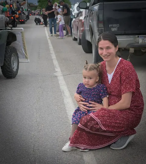 A woman and a young child sit together on a street during an outdoor event.