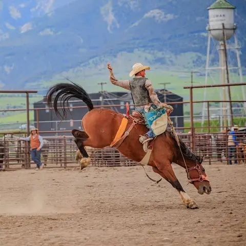 A cowboy rides a bucking horse in an outdoor arena.