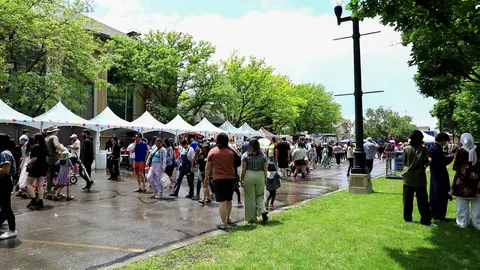 A crowd of people walking along an outdoor market with tents.