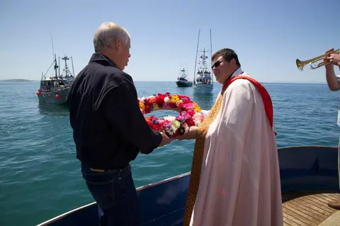 Two men holding a flower wreath on a boat.