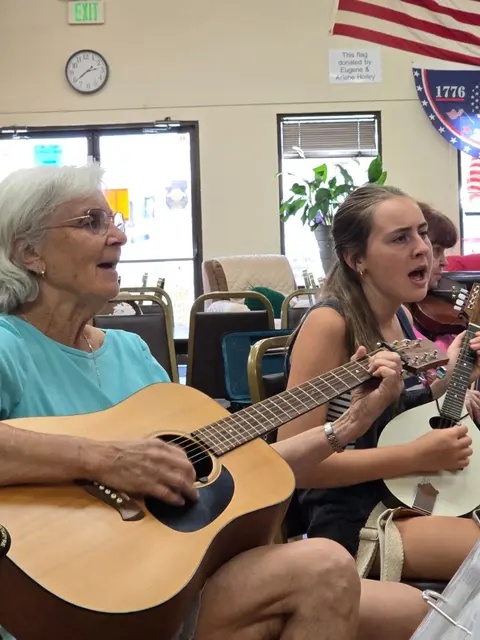 People playing acoustic guitars and singing together indoors.