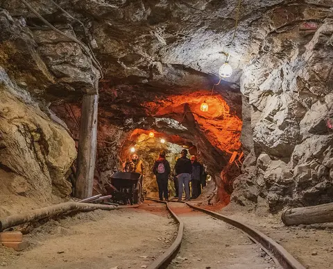 People walking through an underground mine with tracks on the floor.
