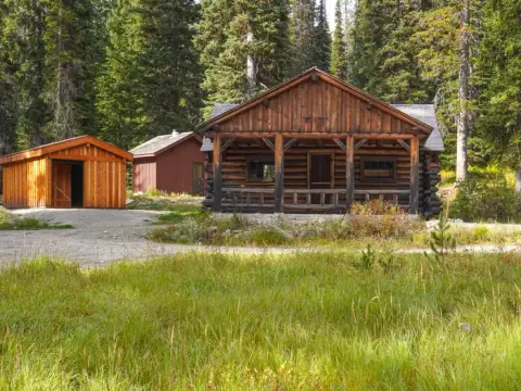 A rustic wooden cabin and outbuildings surrounded by forest.