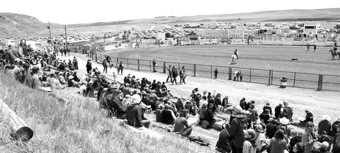 A black and white photo of a large crowd watching an event at a rural arena.