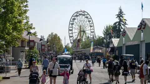 A Ferris wheel rises over a crowded fairground pathway filled with people and golf carts.