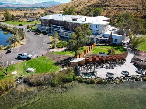An aerial view of a large brick resort building situated next to a lake and rolling hills.