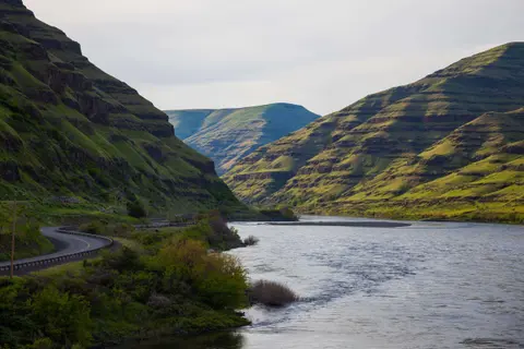 A winding road runs beside a river flowing through a lush green canyon.