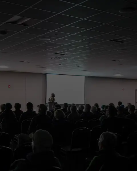 A speaker addresses a large audience seated in a conference room.